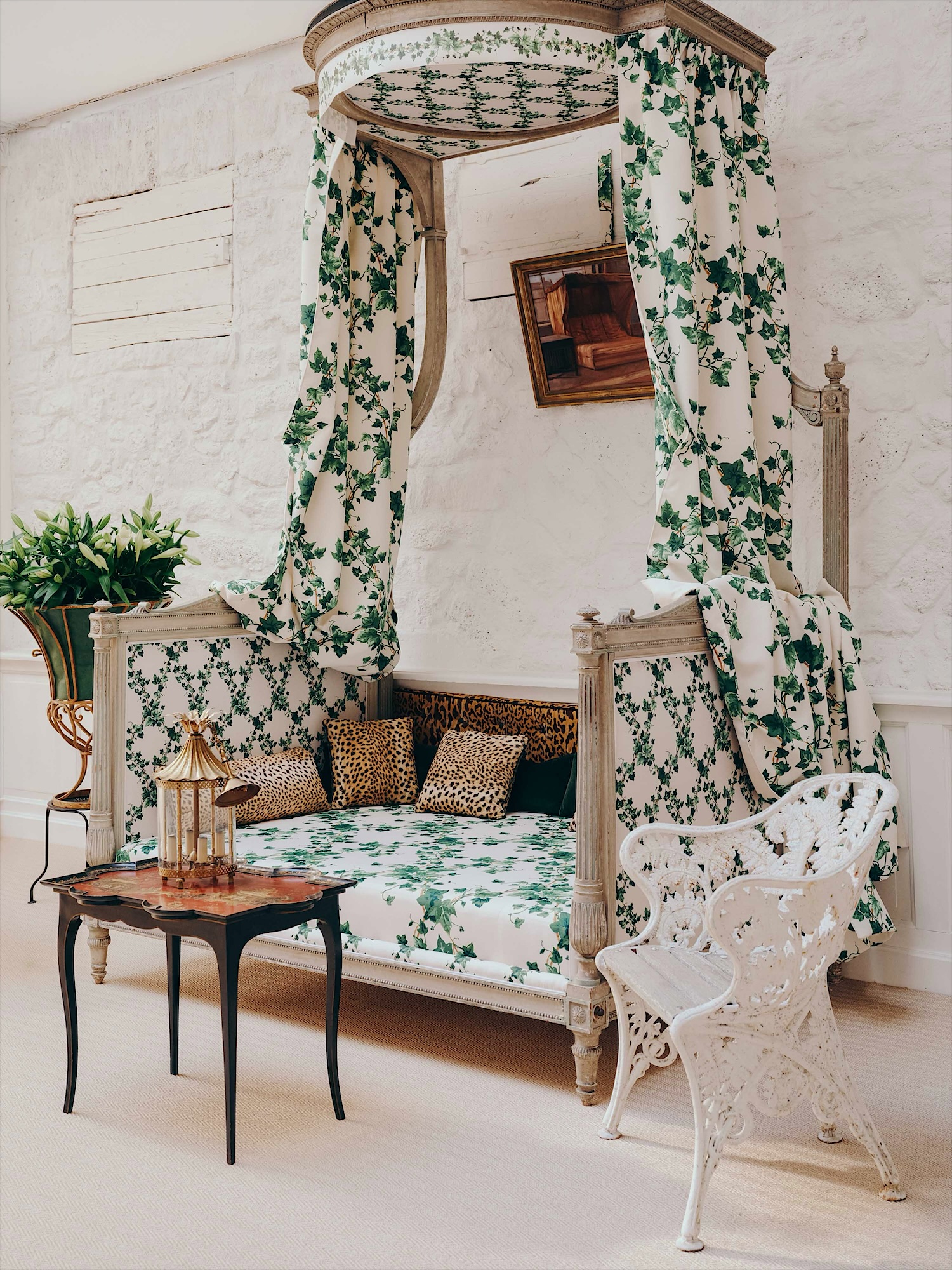 Canopy bed hung with ivy-print fabric, a white cast-iron garden armchair and a black lacquered side table